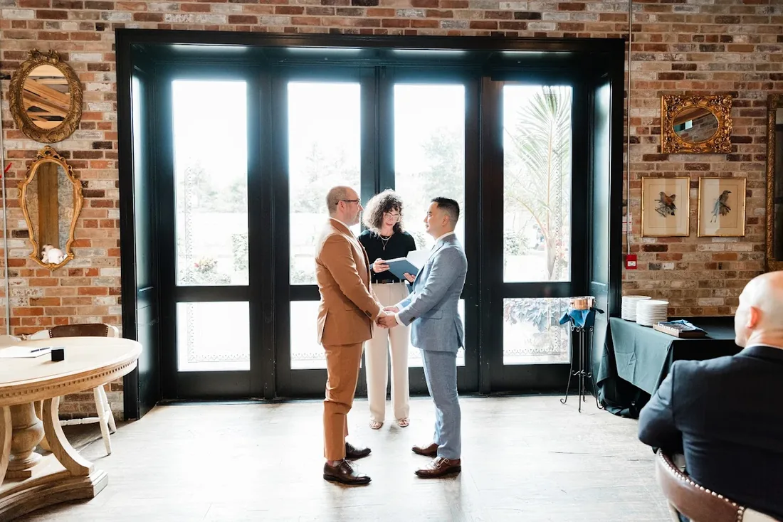 Two grooms holding hands during their ceremony as Charity officiates