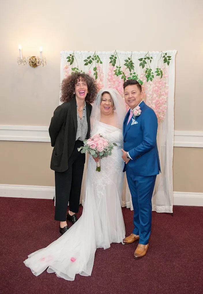 Charity celebrating with a newlywed couple beside their floral backdrop