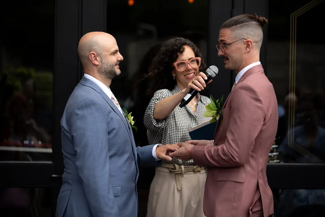 Charity officiating as two grooms exchange rings